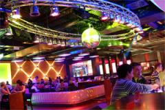 Die Leute sitzen an Tischen und einer Bar in einem lebhaften, farbenfrohen Nachtclub mit Neonlicht, einer Discokugel und modernem Dekor.