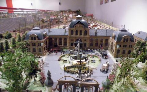 Modellbahnhof mit detaillierten Gebäuden, einem Springbrunnen, Pferdekutschen, Bäumen und Miniaturfiguren in einem naturgetreuen Diorama.