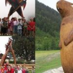 Kinder posieren in Gruppen neben großen hölzernen Tierskulpturen im Freien, mit Bergen und Grünflächen im Hintergrund.