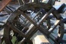 Nahaufnahme eines hölzernen Wasserrads, auf dessen Struktur das Sonnenlicht Schatten wirft und unter dem Wasser fließt.