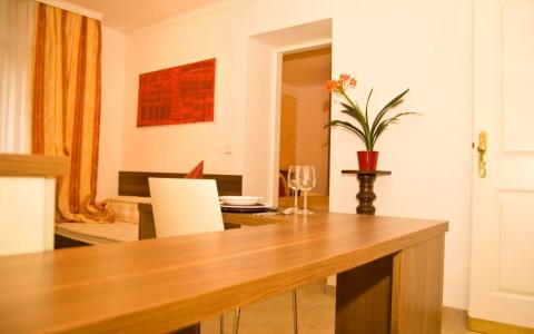 Ein moderner Essbereich mit einem Holztisch, weißen Stühlen, einem roten Gemälde an der Wand und einer Topfpflanze auf einem kleinen Sockel.