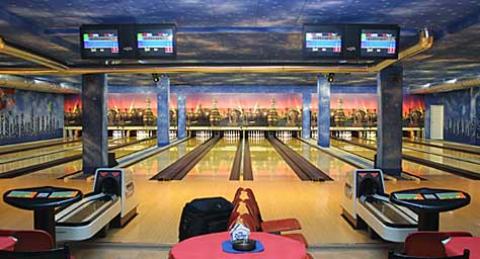 Vier Bowlingbahnen in einer hell erleuchteten Bowlingbahn mit elektronischen Anzeigetafeln über dem Kopf und Sitzbereichen im Vordergrund.