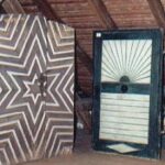 Ein gemusterter Holzschrank und eine Tür mit einem geometrischen Sonnenschliffmuster befinden sich in einem Dachgeschoss mit einer schrägen Holzdecke.