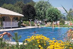 Die Menschen schwimmen und entspannen sich an sonnigen Tagen in einem von Bäumen, Blumen und einem Holzpavillon umgebenen Freibad.