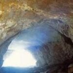Blick aus dem Inneren einer Felsenhöhle auf einen hellen, sonnenbeschienenen Eingang.