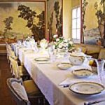 Ein langer, eleganter Esstisch, gedeckt mit feinem Porzellan und floralen Tafelaufsätzen in einem Raum mit malerischen Wandbildern und natürlichem Licht durch ein Fenster.