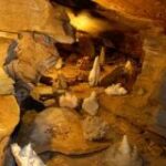 Höhleninneres mit Felsformationen, darunter Stalagmiten und Stalaktiten, beleuchtet durch künstliches Licht.