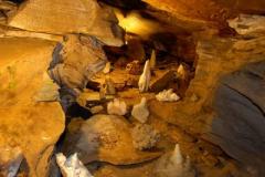 Höhleninneres mit Felsformationen, darunter Stalagmiten und Stalaktiten, beleuchtet durch künstliches Licht.