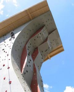 Eine Person klettert an einer künstlichen Kletterwand im Freien mit verschiedenen Griffen, unter einem sonnigen blauen Himmel.