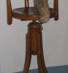 Ein hölzerner Drehstuhl mit einem geschnitzten Tierkopf, möglicherweise ein Pferd, der an der Rückenlehne befestigt ist.