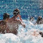 Mehrere Personen schwimmen und spielen in einem Pool, wobei das Wasser um sie herum spritzt.
