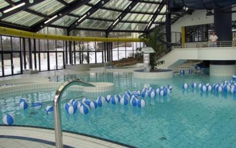 Hallenbad mit vielen blauen und weißen Strandbällen, die auf dem Wasser schwimmen, umgeben von Glaswänden und einem Glasdach.