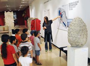 Eine Frau zeigt auf eine Karte an der Wand, während eine Gruppe von Kindern in einem Museum vor ihr steht.