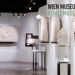Ausstellungsraum im Wien Museum Römermuseum mit antiken Steinartefakten, die auf Wänden und Sockeln unter Galeriebeleuchtung präsentiert werden.