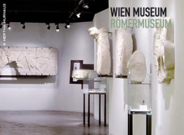 Ausstellungsraum im Wien Museum Römermuseum mit antiken Steinartefakten, die auf Wänden und Sockeln unter Galeriebeleuchtung präsentiert werden.