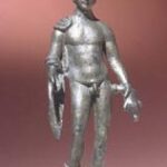 Bronzestatue einer nackten männlichen Figur, die einen geflügelten Helm und Sandalen trägt, ein Schild und einen anderen Gegenstand hält und auf einem kleinen Sockel steht.