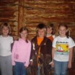 Fünf Kinder stehen Seite an Seite in einer Blockhütte und lächeln in die Kamera.