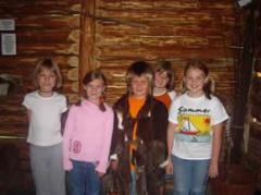 Fünf Kinder stehen Seite an Seite in einer Blockhütte und lächeln in die Kamera.