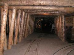 Holzbalken säumen die Wände und die Decke eines unterirdischen Bergwerkstunnels mit Gleisen am Boden.