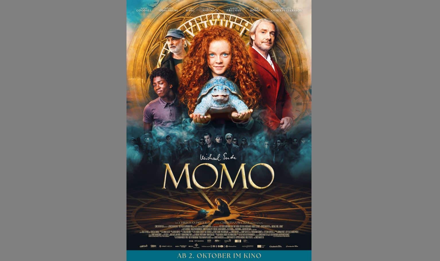 Filmplakat für "Momo" mit einem rotgelockten Mädchen, das eine Schildkröte in der Hand hält, umgeben von vier anderen Figuren, mit einem goldenen Zifferblatt im Hintergrund.