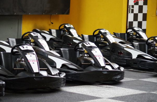 Mehrere schwarz-weiße Go-Karts sind in einer Reihe in einem Innenraum auf einem karierten Boden in der Nähe einer gelben Wand und eines karierten Flaggenmusters geparkt.