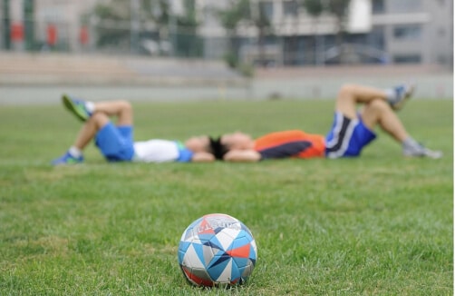 Zwei Personen liegen im Hintergrund auf dem Rasen, während im Vordergrund ein bunter Fußball im Mittelpunkt steht.