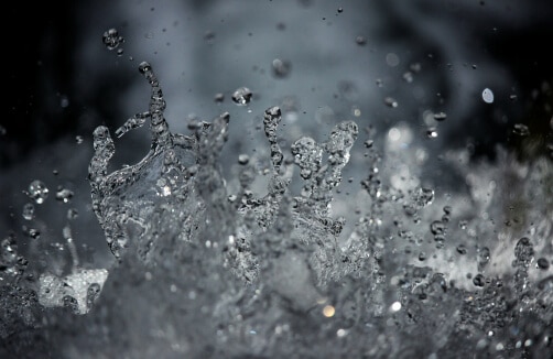 Nahaufnahme von Wassertropfen, die vor einem dunklen, unscharfen Hintergrund in verschiedene Richtungen spritzen und verstreut werden.