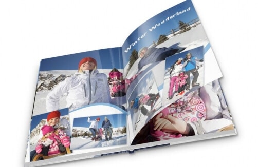 Aufgeschlagenes Fotobuch, das winterliche Szenen mit Menschen in bunter Winterkleidung zeigt, die im Schnee spielen; Text "Winter Wonderland" auf einer Seite.