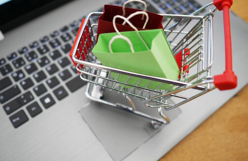 Ein kleiner Einkaufswagen mit bunten Papiertüten steht auf einer Laptop-Tastatur, die für Online-Shopping steht.