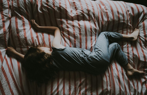 Ein Kind liegt auf einem Bett mit rot-weiß gestreiften Laken und ruht auf der Seite mit ausgestreckten Armen und Beinen.