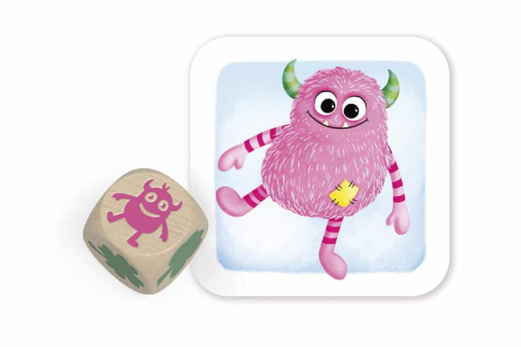 Ein rosafarbenes, flauschiges Monster mit grünen Hörnern und gestreiften Armen und Beinen ist auf einer Karte abgebildet, daneben ein Holzwürfel mit demselben Bild und grünen Punkten.