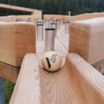 Eine Holzkugel mit der Aufschrift "Alpine Coaster MCI" steht am Anfang einer Holzbahn mit mehreren aufrecht stehenden Metallzylindern im Hintergrund.