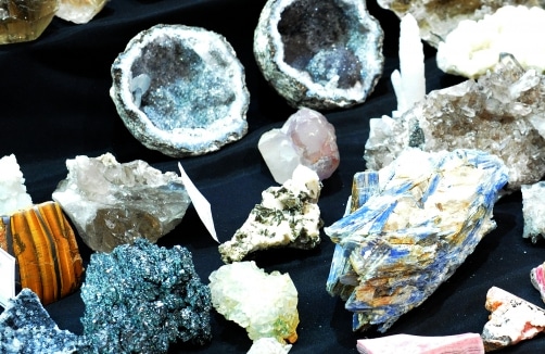 Eine Vielzahl von Mineralien und Kristallen, darunter Geoden, Quarz und andere bunte Steine, ausgestellt auf einer schwarzen Oberfläche.
