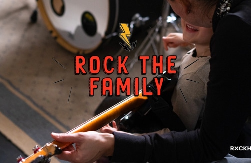 Ein Erwachsener und ein Kind spielen zusammen eine E-Gitarre; der Text auf dem Bild lautet "Rock The Family" mit einer Blitzgrafik über den Worten.