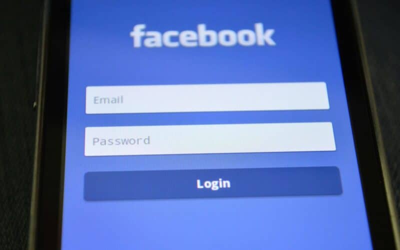 Ein Smartphone-Bildschirm zeigt die Facebook-Anmeldeseite mit Feldern für E-Mail, Passwort und einer blauen Schaltfläche "Anmelden" an.
