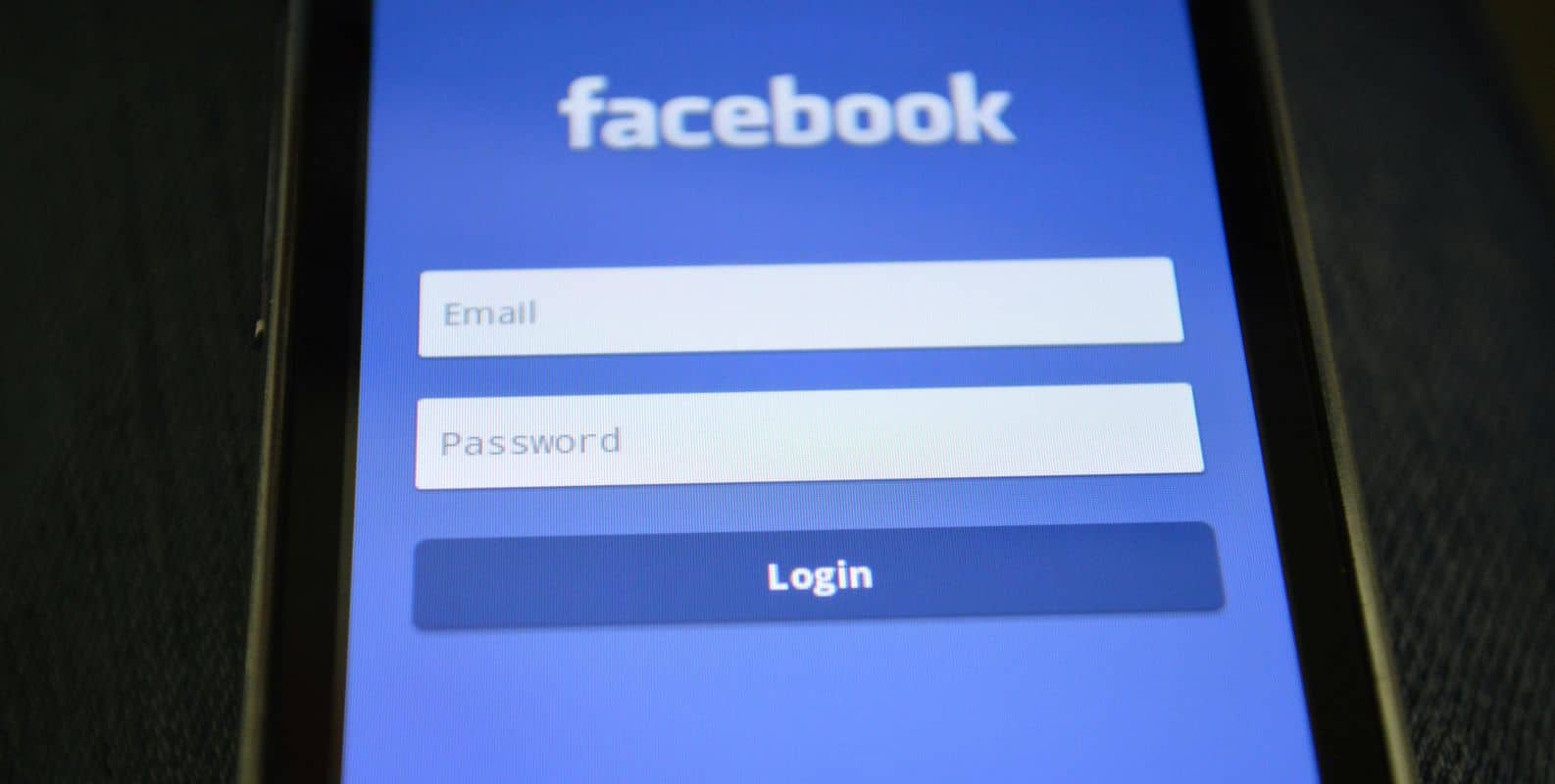 Ein Smartphone-Bildschirm zeigt die Facebook-Anmeldeseite mit Feldern für E-Mail, Passwort und einer blauen Schaltfläche "Anmelden" an.