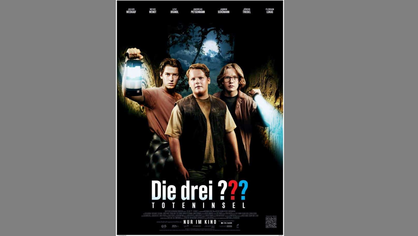 Drei Jungen stehen in einem dunklen Wald und halten Laternen und eine Taschenlampe in der Hand. Unter ihnen ist der Titel "Die drei ??? Toteninsel" steht auf einem Filmplakat unter ihnen.