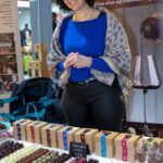 Eine Frau steht auf einem Markt oder einer Veranstaltung hinter einem Tisch mit verschiedenen Pralinen und Pralinenschachteln.
