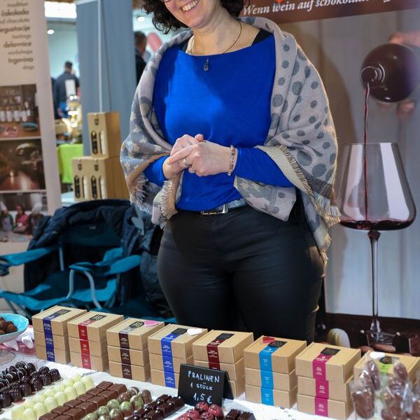 Eine Frau steht auf einem Markt oder einer Veranstaltung hinter einem Tisch mit verschiedenen Pralinen und Pralinenschachteln.