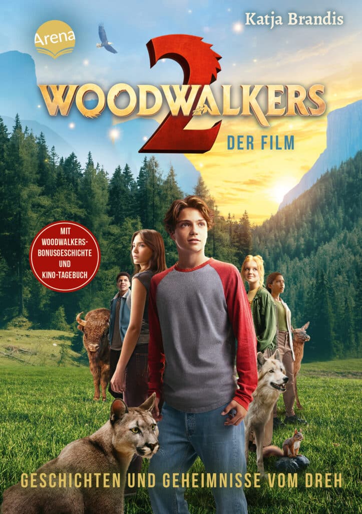 Filmplakat für "Woodwalkers 2" mit einer Gruppe Jugendlicher und Tieren wie einem Wolf, einem Puma und einem Bären, die in einer bewaldeten Berglandschaft stehen.