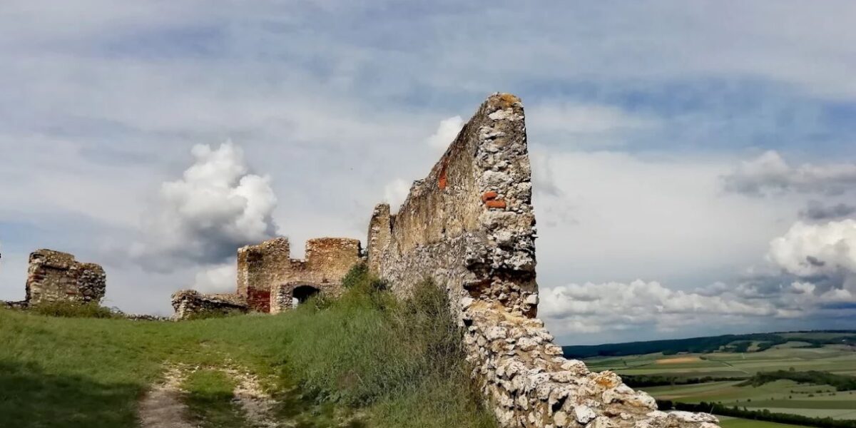 Eine Steinmauer mit einem Steinbogen und Gras auf einem Hügel.