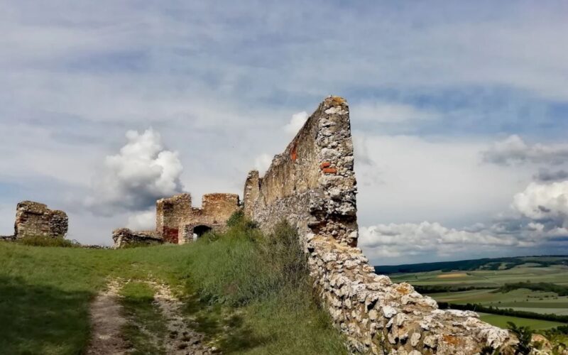 Eine Steinmauer mit einem Steinbogen und Gras auf einem Hügel.