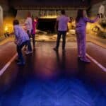 Fünf Personen mit Virtual-Reality-Headsets in einem Raum mit altägyptischem Dekor, darunter Statuen, Sarkophage und Hieroglyphen an den Wänden.