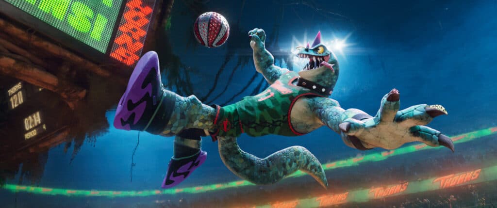 Ein cartoonhaftes, echsenartiges Wesen in einem Basketballtrikot springt in einer animierten Stadionkulisse, um einen Basketball in der Luft zu fangen.
