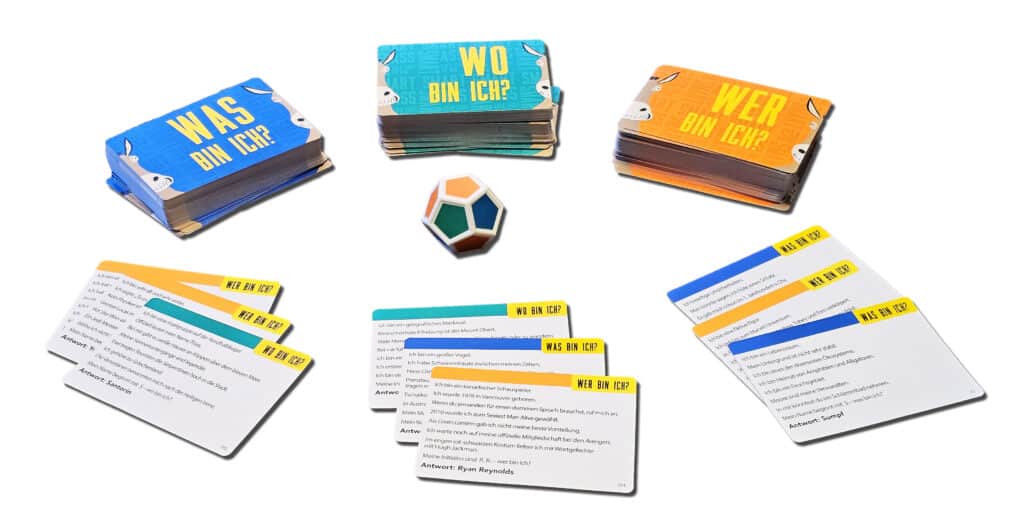 Drei Kartenstapel in deutscher Sprache mit den Aufschriften "WAS BIN ICH?", "WO BIN ICH?" und "WER BIN ICH?", ein 12-seitiger Würfel und mehrere Karten auf weißem Hintergrund.