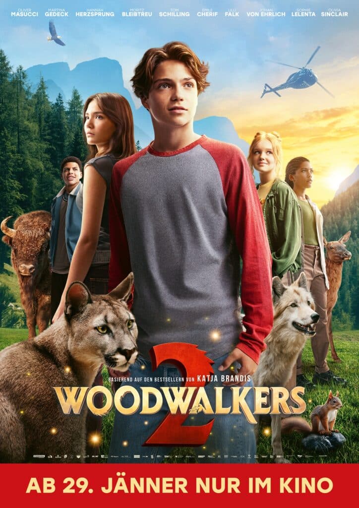Eine Gruppe von Teenagern steht in einer malerischen Waldlandschaft mit wilden Tieren, darunter Wölfe und ein Puma. Der Filmtitel "Woodwalkers 2" wird unten mit einem deutschen Erscheinungsdatum angezeigt.