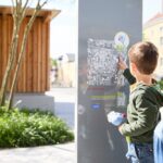 Ein kleiner Junge zeigt auf eine Karte auf einer Informationstafel im Freien, während ein Erwachsener neben ihm steht.