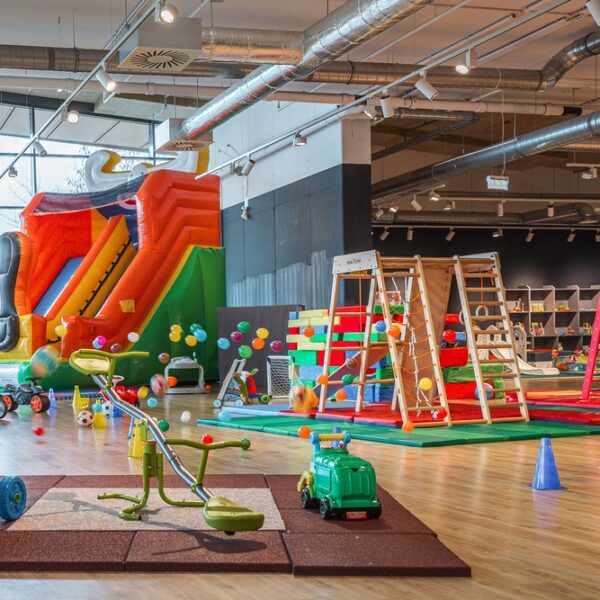 Indoor-Kinderspielbereich mit einer großen aufblasbaren Rutsche, Klettergerüsten, Aufsitzspielzeug, weichen Spielgeräten und farbenfroher Dekoration auf einem Holzboden.