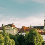 Ein großer historischer Gebäudekomplex mit einer hohen Kirche mit zwei spitzen Türmen, umgeben von Bäumen unter einem klaren Himmel.