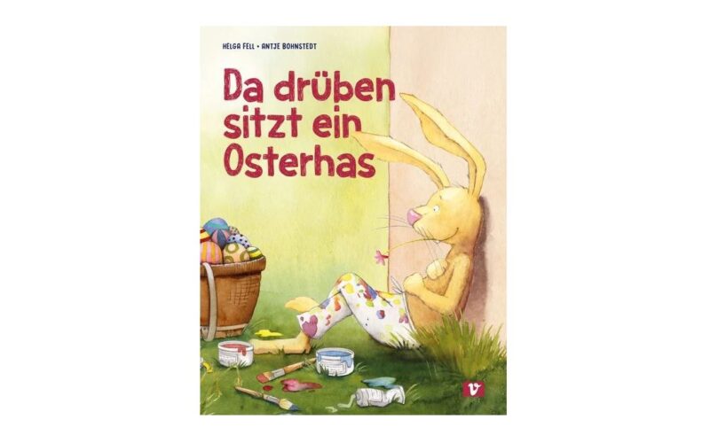 Ein gelber Hase sitzt an einem Baum und hält Nadel und Faden neben einem Korb mit Ostereiern und bunten Farben. Auf dem Buchdeckel steht "Da drüben sitzt ein Osterhas.
